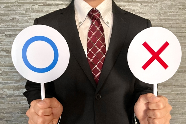 〇とバツの札を持つ男性